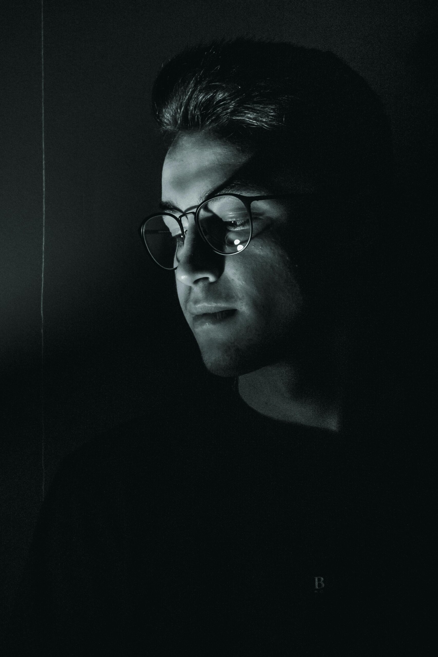 Stylish black and white portrait of a man wearing eyeglasses in low light.