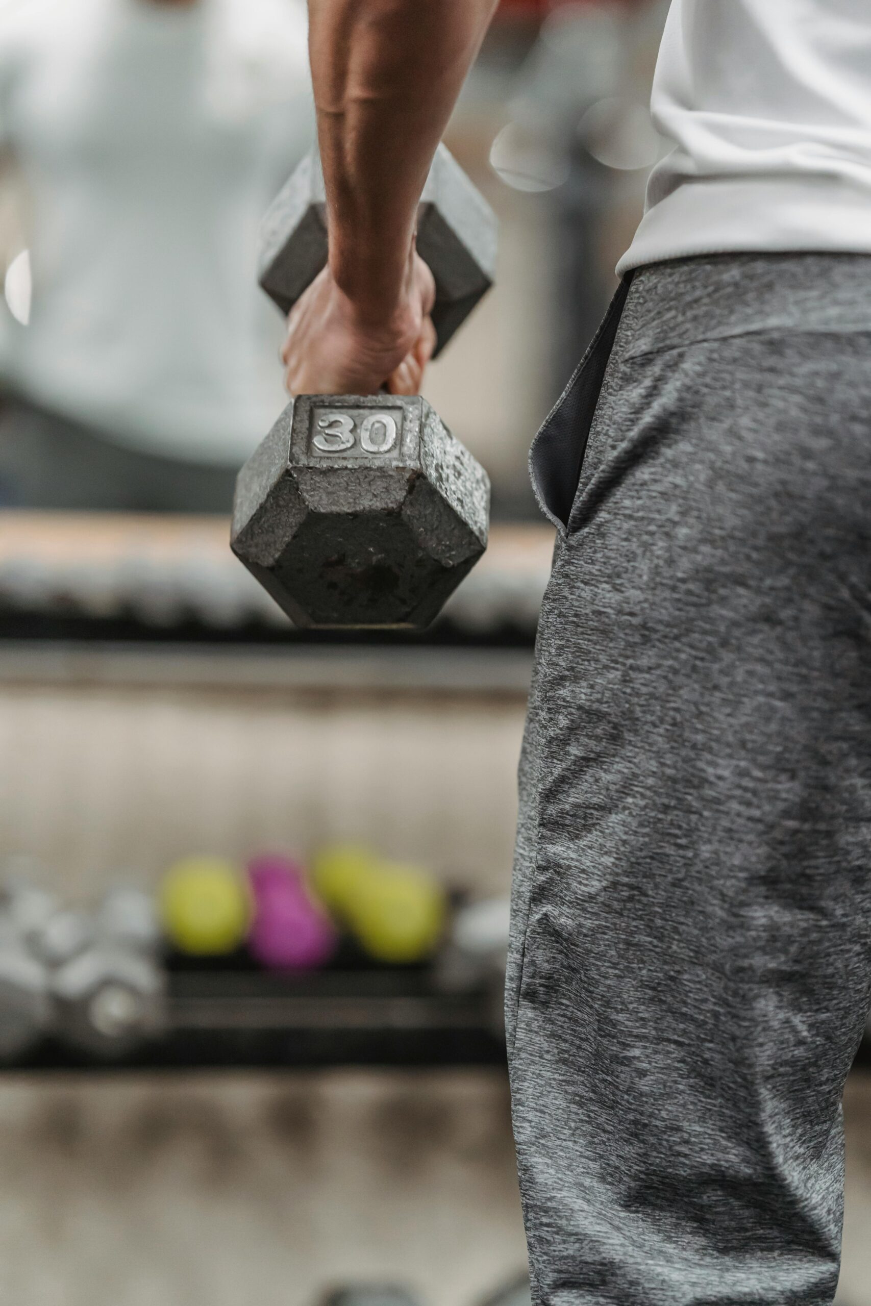 Focused shot of a man lifting a 30-pound dumbbell in a gym environment.