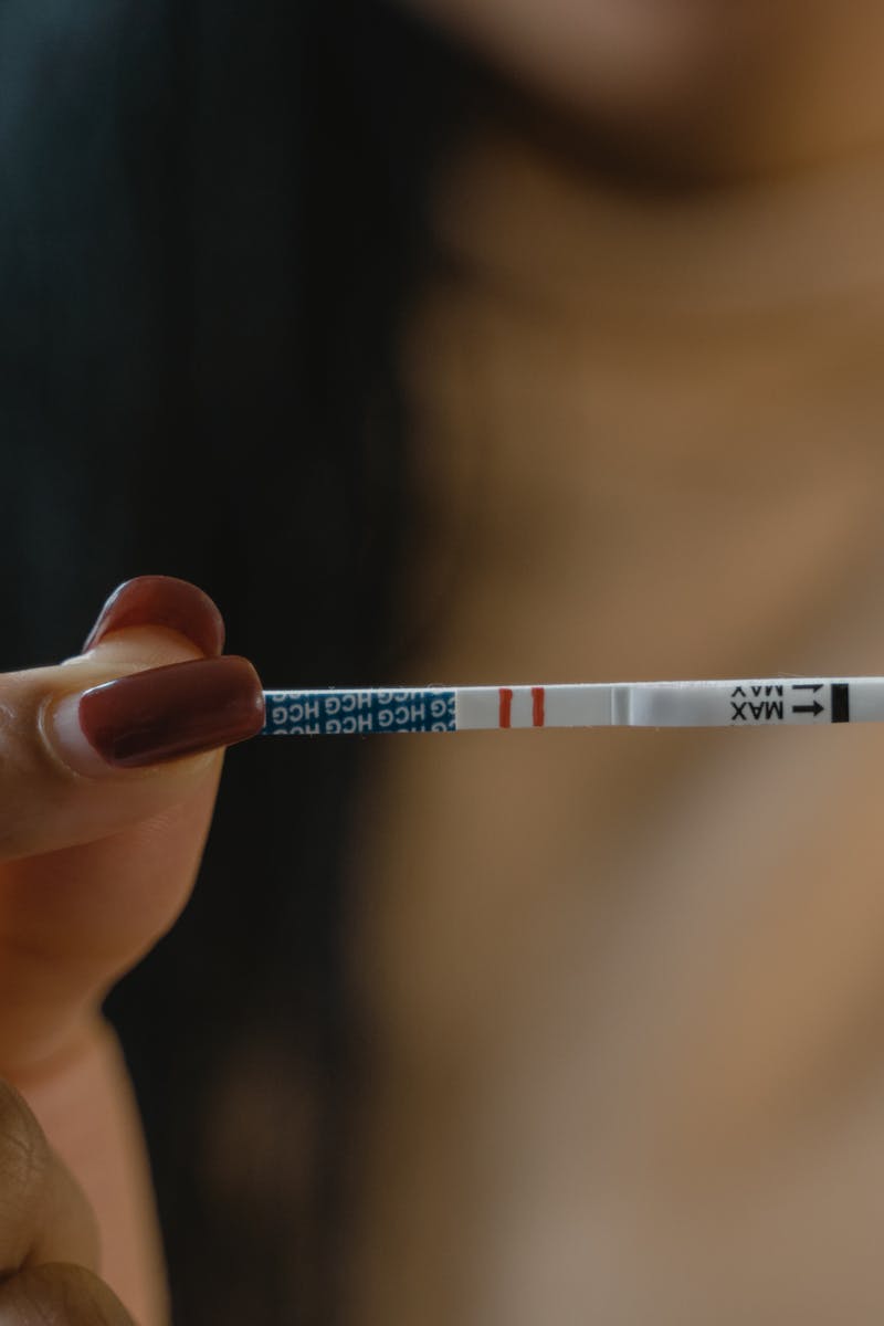 A hand holds a positive pregnancy test strip against a blurred background, symbolizing new beginnings.